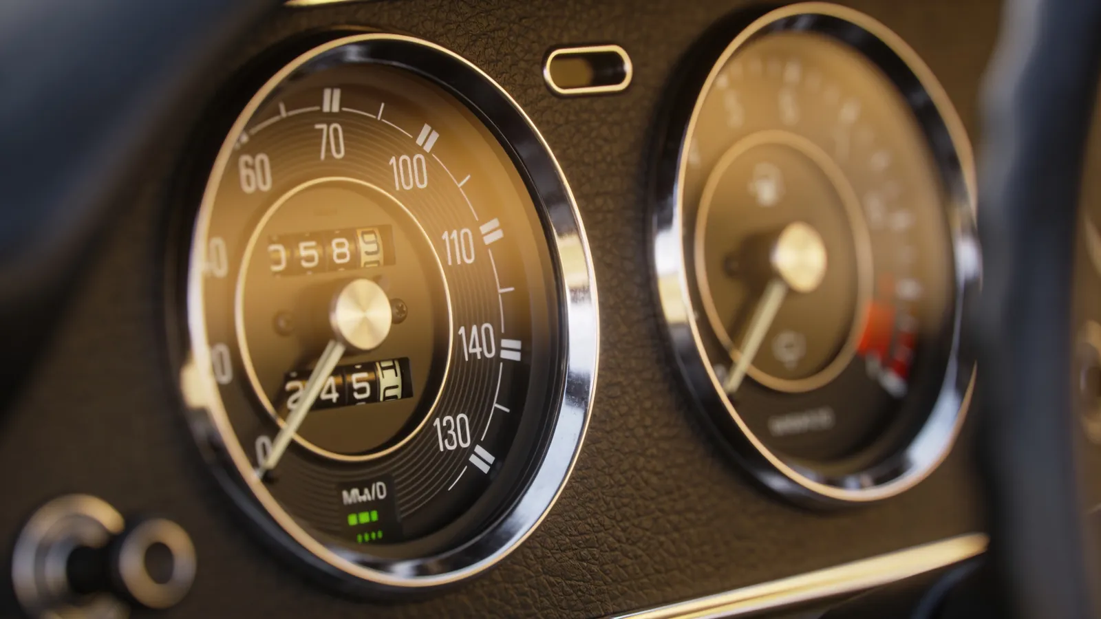 Close-up of a car dashboard with a speedometer and a fuel gauge in warm light