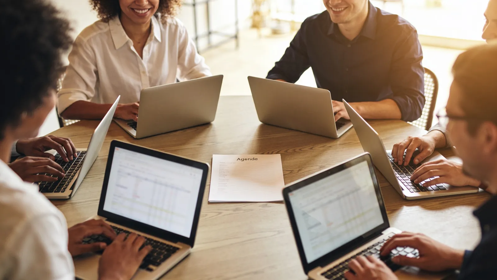A small leadership team in a monthly review around a round table with laptops and a single printed agenda