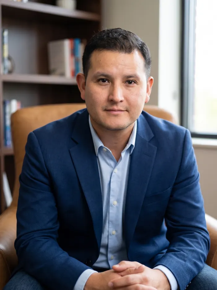 Dennis Alejo seated in a leather chair with bookshelves behind